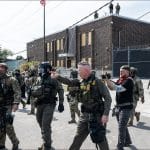 Border Patrol Commander Gregory Bovino in tactical vest walks with armed law enforcement and military personnel outside Broadview, Illinois, ICE detention facility