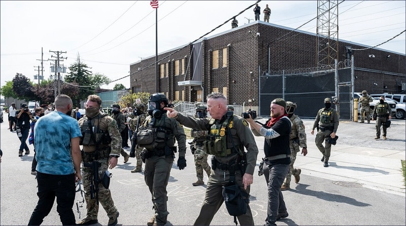Border Patrol Commander Gregory Bovino in tactical vest walks with armed law enforcement and military personnel outside Broadview, Illinois, ICE detention facility