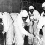 Four workers in full protective suits and respirators clean radioactive contamination inside Three Mile Island auxiliary building, October 1979
