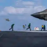 F-35C Lightning II launches from flight deck of aircraft carrier USS Abraham Lincoln as deck crew in yellow and green jerseys work nearby