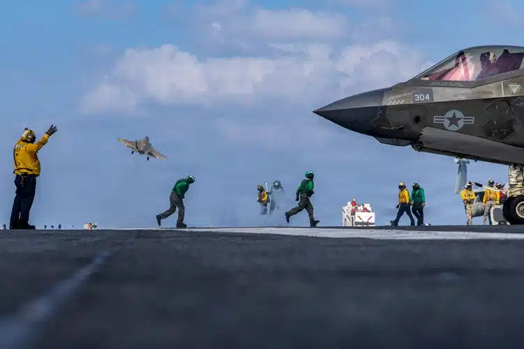 F-35C Lightning II launches from flight deck of aircraft carrier USS Abraham Lincoln as deck crew in yellow and green jerseys work nearby