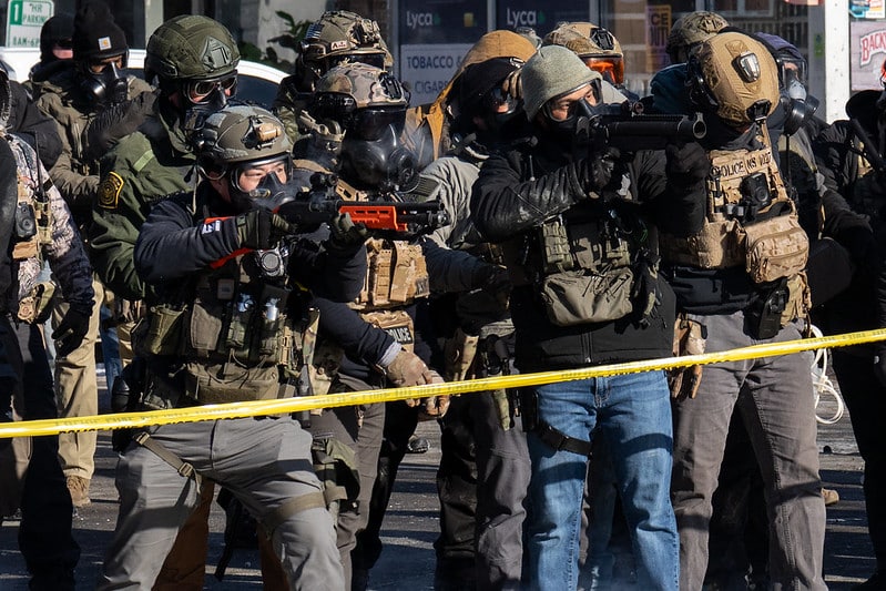 Federal agents in tactical gear with gas masks aim less lethal launchers behind yellow caution tape in Minneapolis