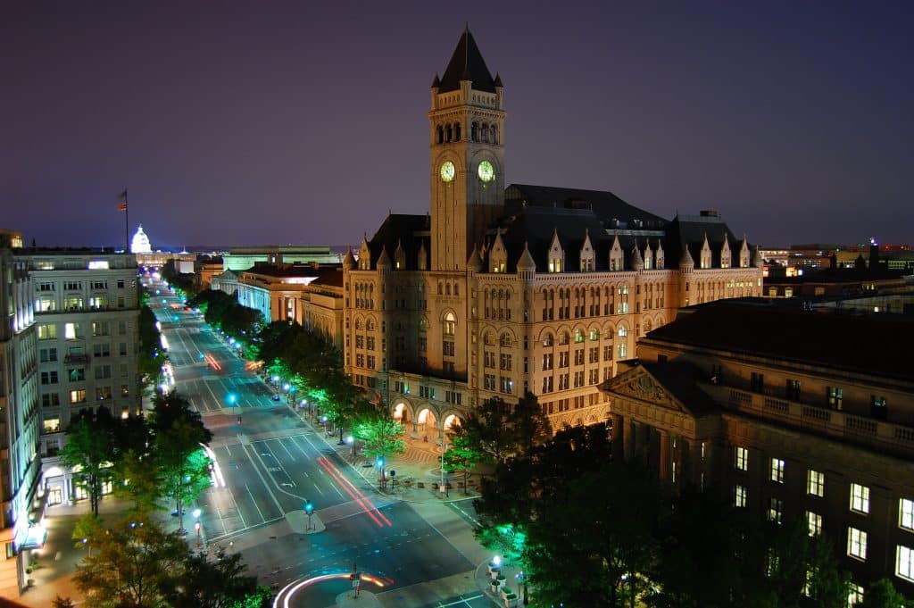 Old Post Office Pavilion and its clock tower illuminated at night on Pennsylvania Avenue in Washington DC with the US Capitol visible in the distance