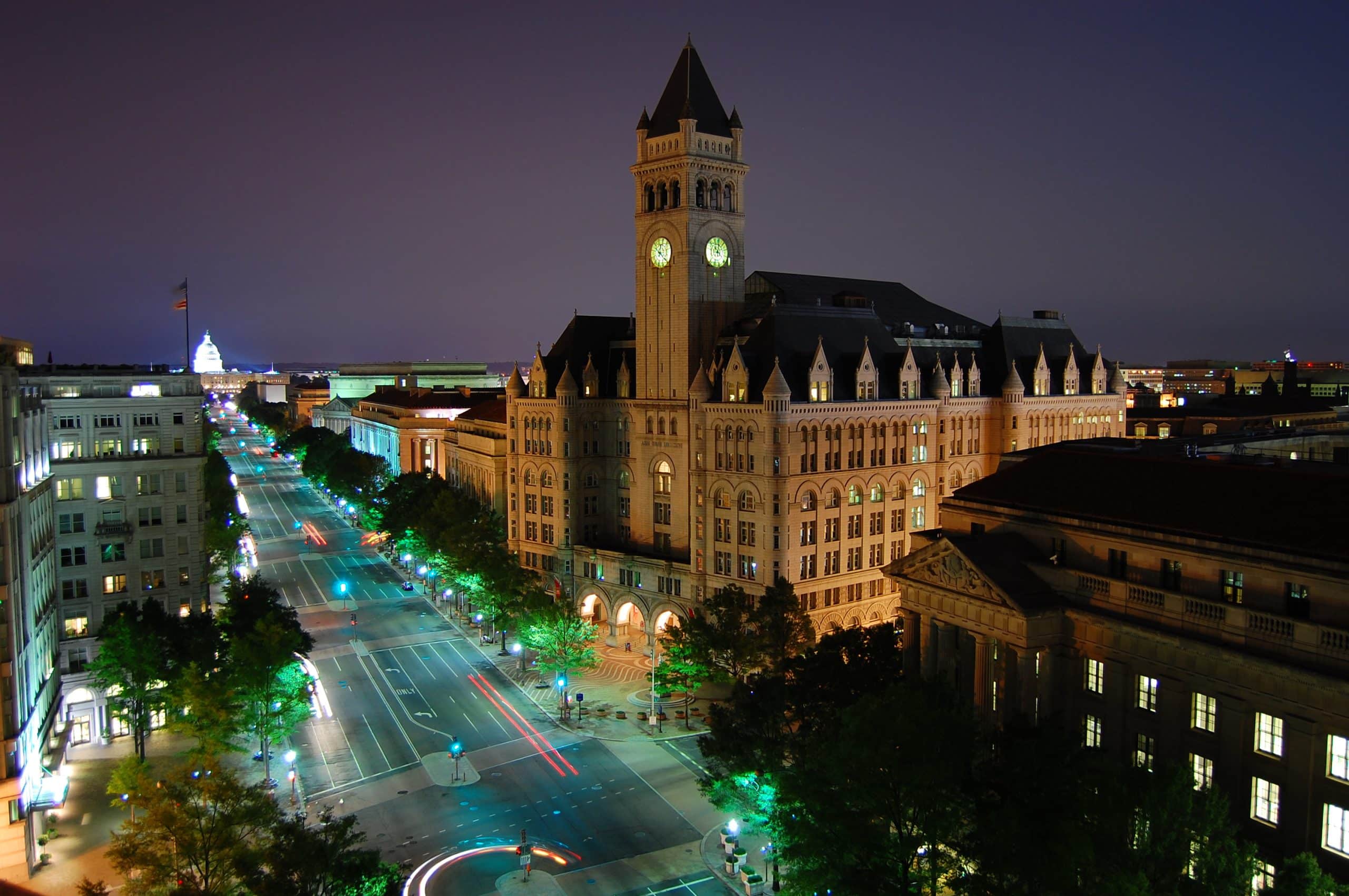 Old Post Office Pavilion and its clock tower illuminated at night on Pennsylvania Avenue in Washington DC with the US Capitol visible in the distance