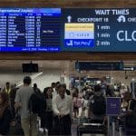 Crowded terminal at Daniel K. Inouye International Airport in Honolulu with digital sign showing Checkpoint 1A closed and passengers waiting near departure board