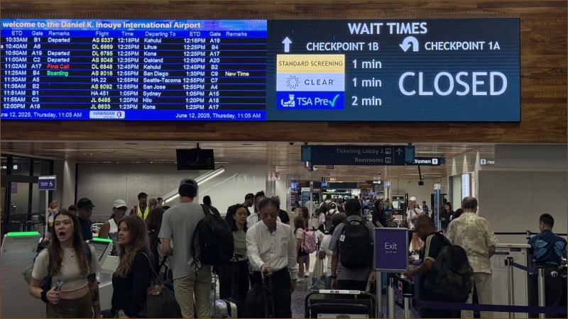 Crowded terminal at Daniel K. Inouye International Airport in Honolulu with digital sign showing Checkpoint 1A closed and passengers waiting near departure board