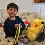 Five-year-old Liam Conejo Ramos sits on a couch surrounded by stuffed animals and a Pikachu plush toy after returning home to Minnesota from ICE detention in Dilley, Texas.