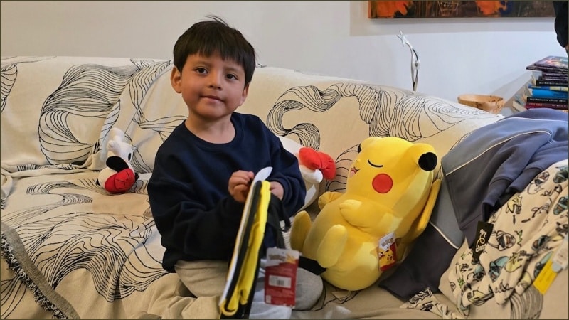 Five-year-old Liam Conejo Ramos sits on a couch surrounded by stuffed animals and a Pikachu plush toy after returning home to Minnesota from ICE detention in Dilley, Texas.
