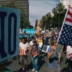 Protesters march through downtown Los Angeles carrying a large "NO" sign and American flag during the No Kings Day of Nonviolent Action, March 28, 2026.