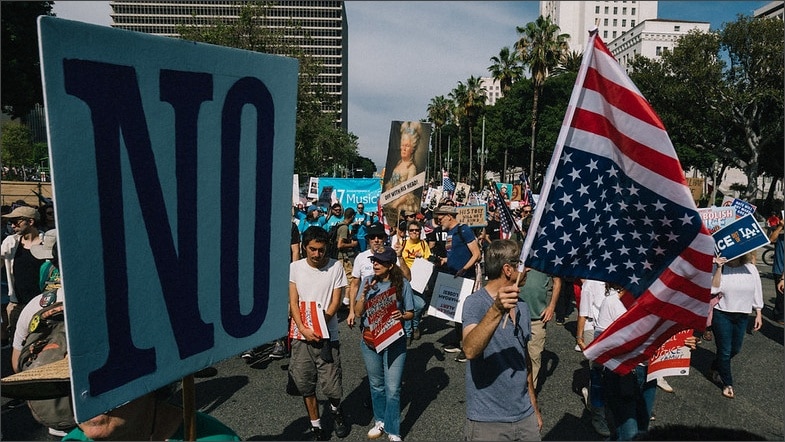 Protesters march through downtown Los Angeles carrying a large "NO" sign and American flag during the No Kings Day of Nonviolent Action, March 28, 2026.
