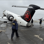 NTSB investigators walk around a damaged Air Canada Express plane with collapsed landing gear on the tarmac at LaGuardia Airport