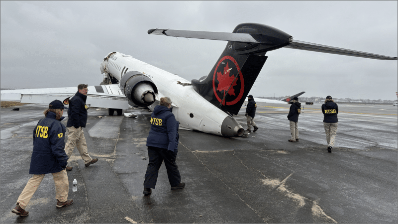 NTSB investigators walk around a damaged Air Canada Express plane with collapsed landing gear on the tarmac at LaGuardia Airport