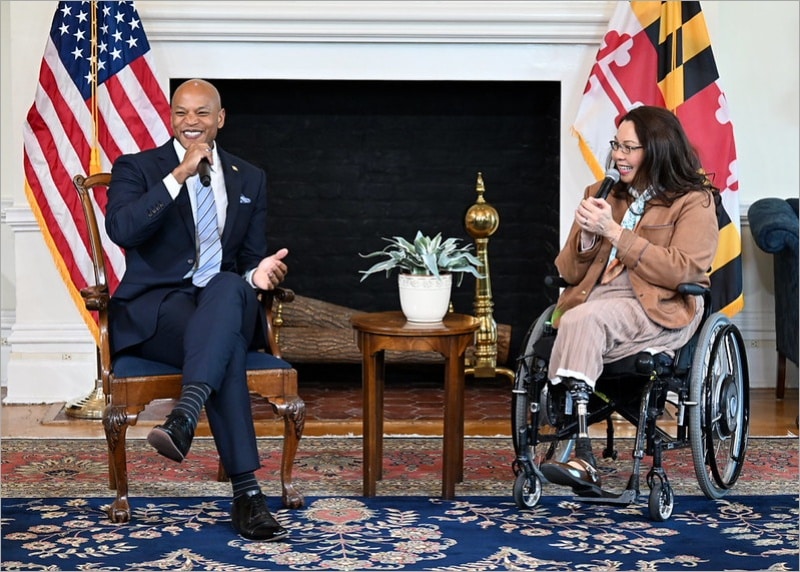 Sen. Tammy Duckworth laughing in her wheelchair next to Maryland Gov. Wes Moore in the Governor's Reception Room in Annapolis