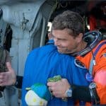 NASA astronaut Reid Wiseman in orange flight suit hugs flight surgeon Richard Scheuring on the flight deck of USS John P. Murtha after Artemis II splashdown in the Pacific Ocean