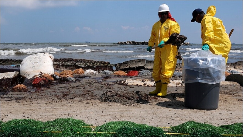 BP cleanup workers in yellow hazmat suits remove oil from Port Fourchon beach during 2010 Deepwater Horizon spill cleanup