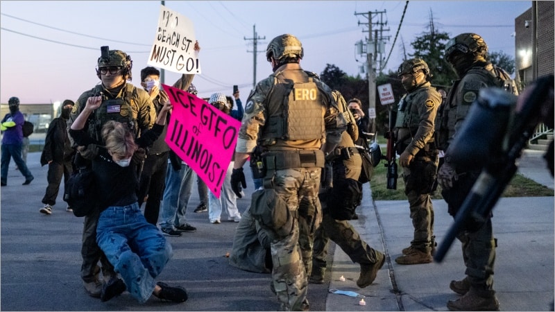 An armed federal ERO agent in tactical gear drags a limp protester by the arms outside the Broadview USCIS Processing Center in Illinois as demonstrators hold signs reading ICE GTFO of Illinois