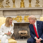 Italian Prime Minister Giorgia Meloni and President Donald Trump sitting together in yellow armchairs by the Oval Office fireplace smiling at each other
