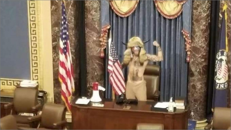 Jacob Chansley, the QAnon Shaman, in horned headdress raises fist at the Senate dais during the January 6, 2021 Capitol attack