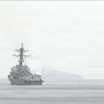 U.S. Navy destroyer transiting the hazy Strait of Hormuz near the Iranian coast