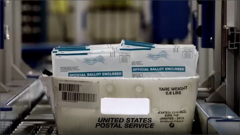 Tray of official mail-in ballot envelopes moving along a U.S. Postal Service sorting line