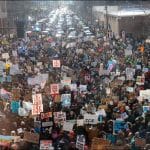 Large crowd of protesters filling a downtown Minneapolis street, many holding hand-lettered ICE OUT signs, January 2026.