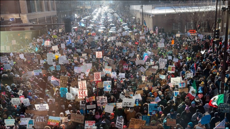 Large crowd of protesters filling a downtown Minneapolis street, many holding hand-lettered ICE OUT signs, January 2026.