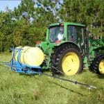 A green tractor sprays glyphosate herbicide across a field of bahiagrass