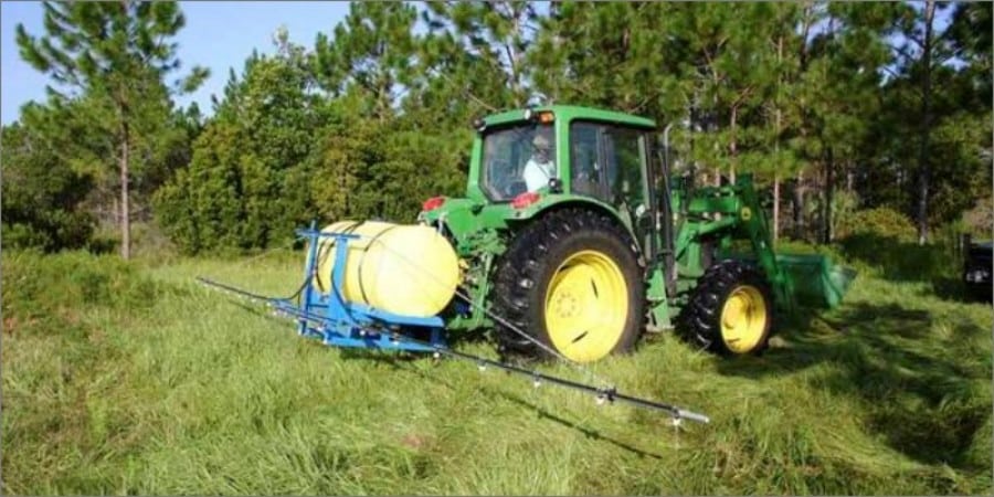 A green tractor sprays glyphosate herbicide across a field of bahiagrass
