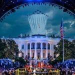 A UFC cage stands on the White House South Lawn under blue lights with a fighter jet flyover during Trump's 80th birthday event