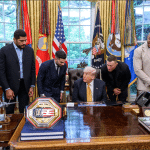 President Donald Trump seated at the Oval Office desk with mixed martial arts fighters and a UFC championship belt, May 2026.