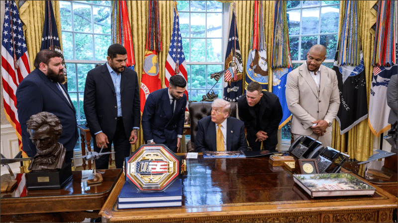 President Donald Trump seated at the Oval Office desk with mixed martial arts fighters and a UFC championship belt, May 2026.