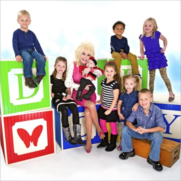 Dolly Parton seated among young children on oversized alphabet blocks promoting the Imagination Library free book program