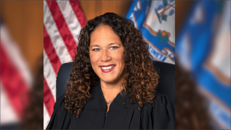 Judge Melanie Cradle in her official portrait, wearing black judicial robes before the American and Connecticut state flags