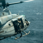 U.S. Marines aboard a UH-1Y Venom helicopter flying over open water near the amphibious assault ship USS Boxer in the Middle East