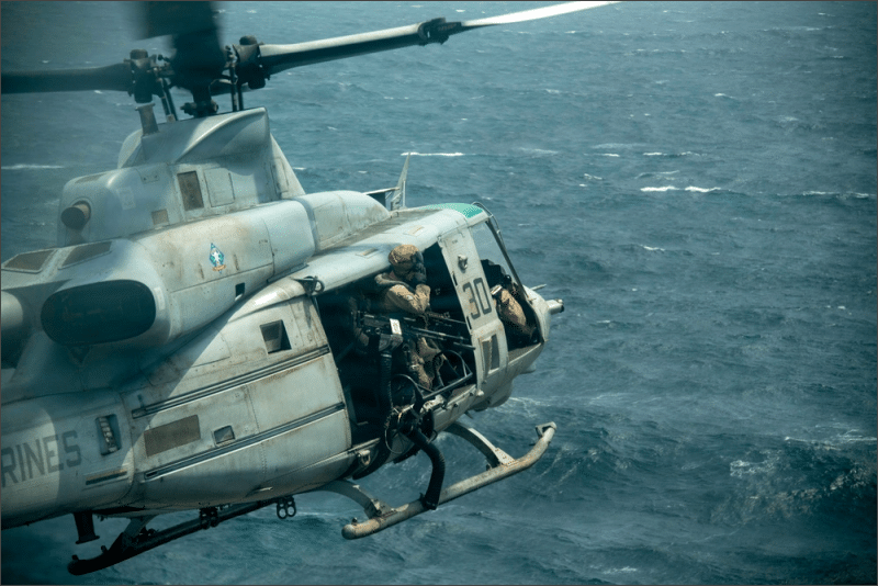 U.S. Marines aboard a UH-1Y Venom helicopter flying over open water near the amphibious assault ship USS Boxer in the Middle East