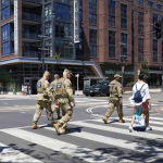 National Guard soldiers in camouflage cross a city street alongside civilian pedestrians near a Whole Foods in Washington, DC