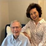 Sen. Mitch McConnell seated with a neck pillow as Elaine Chao stands beside him in a photo released during his rehab stay.