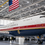 The VC-25B bridge Air Force One aircraft in red, white, and navy presidential livery inside a hangar at Joint Base Andrews beneath an American flag