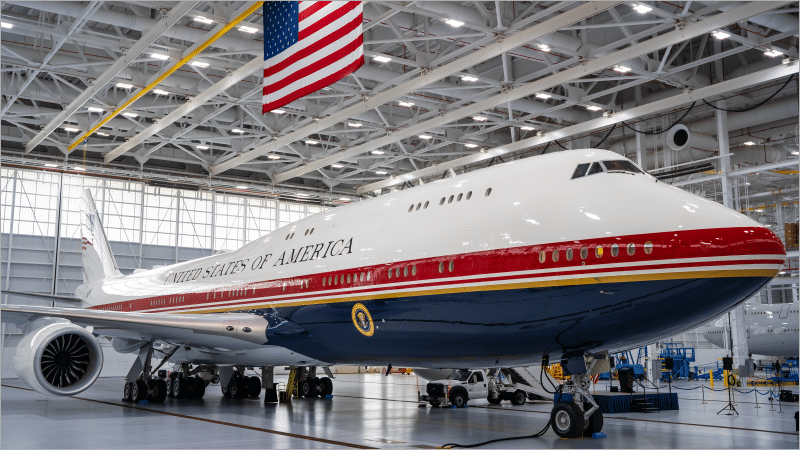 The VC-25B bridge Air Force One aircraft in red, white, and navy presidential livery inside a hangar at Joint Base Andrews beneath an American flag