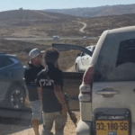 Two Israeli settlers, one carrying a rifle, stand among vehicles on a dirt road in the West Bank where Rep. Ro Khanna's congressional delegation was detained.