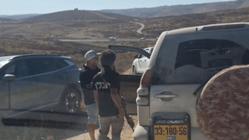 Two Israeli settlers, one carrying a rifle, stand among vehicles on a dirt road in the West Bank where Rep. Ro Khanna's congressional delegation was detained.