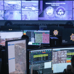 Analysts at computer workstations inside the Las Vegas fusion center, surrounded by a wall of surveillance video monitors