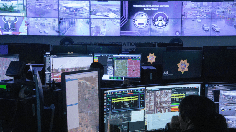 Analysts at computer workstations inside the Las Vegas fusion center, surrounded by a wall of surveillance video monitors