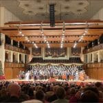 Packed Kennedy Center Concert Hall audience watching the annual Messiah sing-along with orchestra, chorus, and Christmas trees on stage