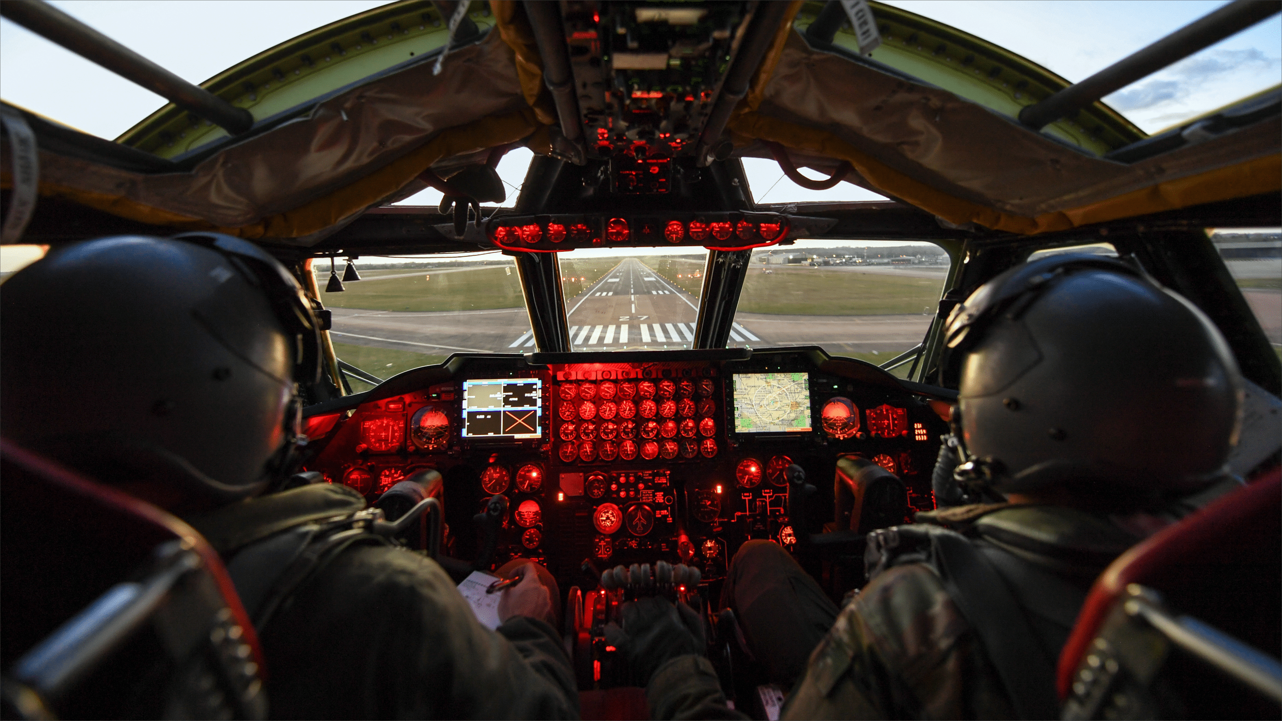Two Air Force pilots in a red-lit B-52 cockpit approach the runway at RAF Fairford, England.