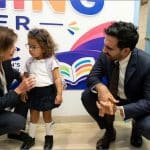 Gov. Kathy Hochul and Mayor Zohran Mamdani crouch beside a toddler in a school uniform at a Manhattan 2-K childcare provider on opening day.
