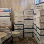 Stacks of white file boxes piled beside a toilet and marble sink in a gilded Mar-a-Lago bathroom