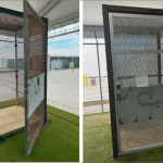 Empty 18-square-foot metal mesh cage on artificial turf inside a fenced yard at the Alligator Alcatraz detention site in Florida