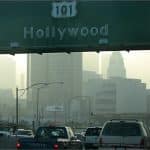 Smoggy downtown Los Angeles skyline behind a US Route 101 Hollywood highway sign over heavy traffic