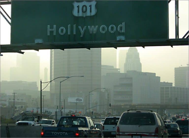 Smoggy downtown Los Angeles skyline behind a US Route 101 Hollywood highway sign over heavy traffic